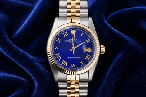 Luxury watch with blue face and gold accents on a blue fabric background