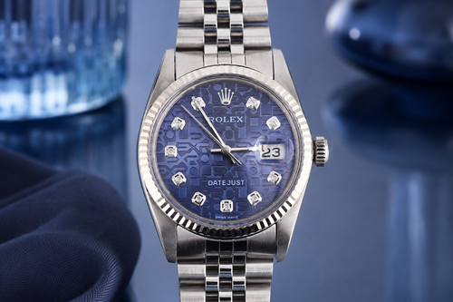 Silver Rolex watch with blue face on a reflective surface