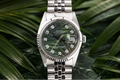 Silver watch with a green dial on a leafy background