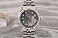 Silver watch with a dark face on a sandy surface