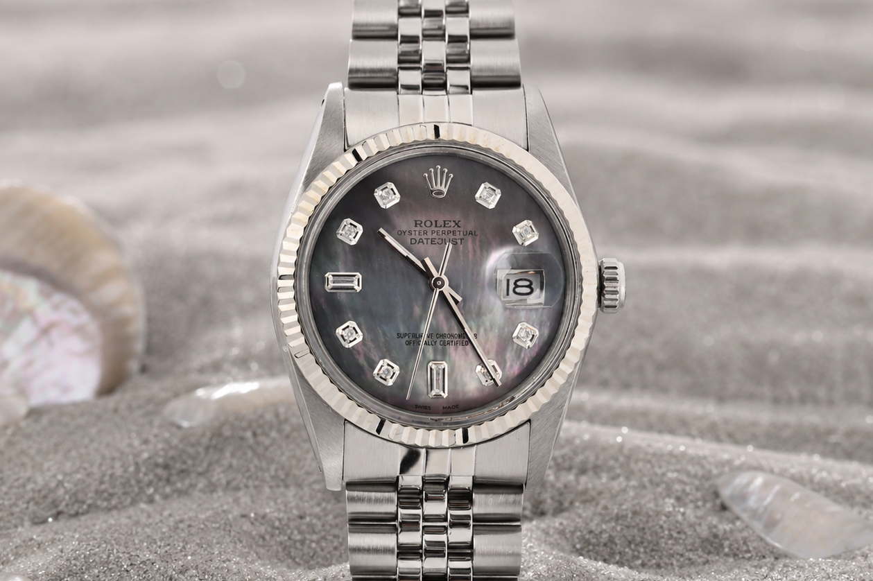 Silver watch with a dark face on a sandy surface