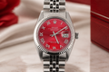 Silver watch with a red face on a light wooden surface