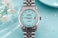 Silver watch with a turquoise dial on a light blue background with white flowers