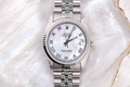 Silver Rolex watch with a white face on a textured white background