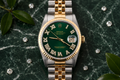 Luxury watch with green dial and gold and silver band on a dark marble surface with decorative elements.