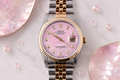 Rolex watch with pink face and gold accents on a marble surface with seashells.