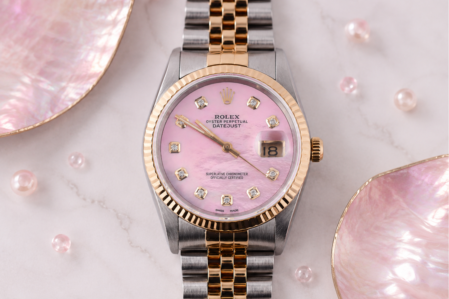 Rolex watch with pink face and gold accents on a marble surface with seashells.