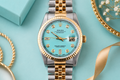 Luxury watch with turquoise dial and gold and silver band on a light blue background