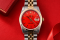 Luxury watch with red face and gold and silver band on a red background
