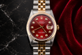 Luxury watch with a red face and gold accents on a dark marble and red fabric background