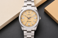 Silver Rolex watch with a beige dial on a dark surface with a beige box.