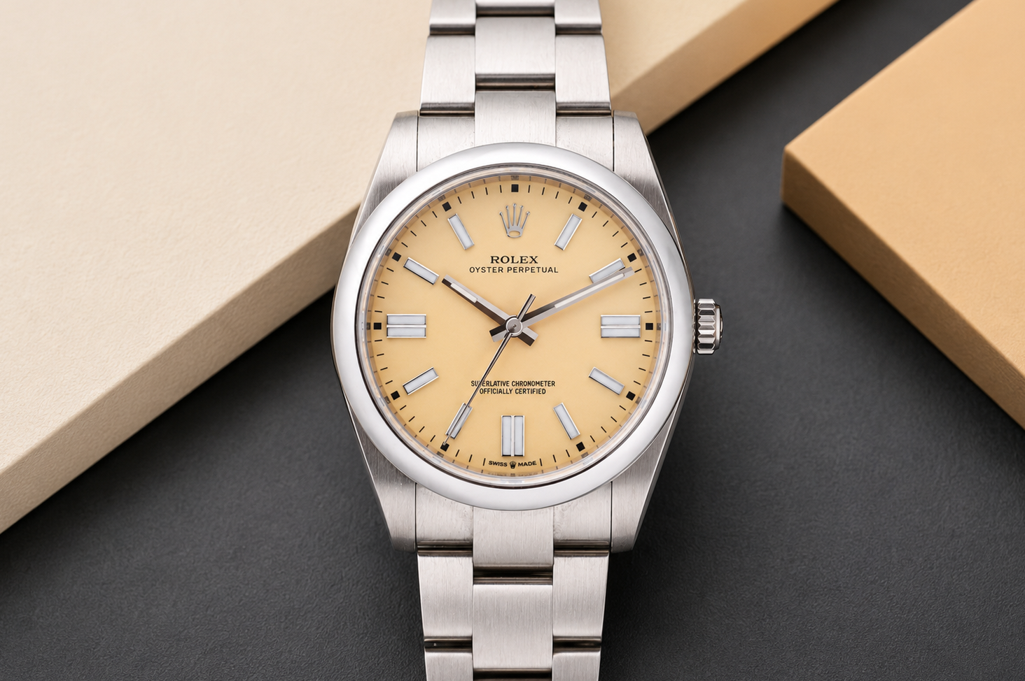 Silver Rolex watch with a beige dial on a dark surface with a beige box.