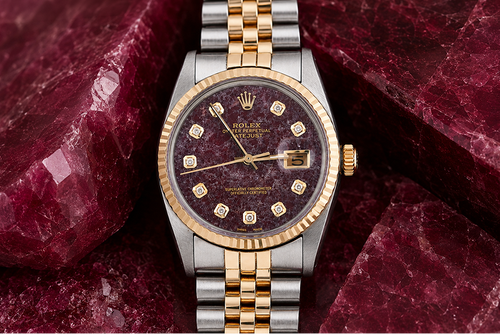 Luxury watch with a maroon face and gold accents on a red stone background