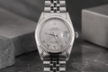 Silver Rolex watch on a dark surface with a gray background