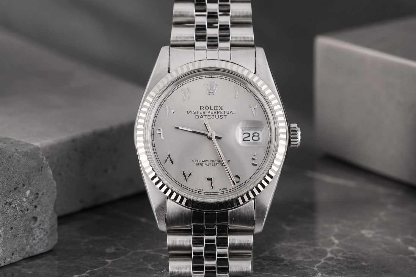 Silver Rolex watch on a dark surface with a gray background