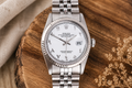 Silver Rolex watch on a wooden surface with a neutral background