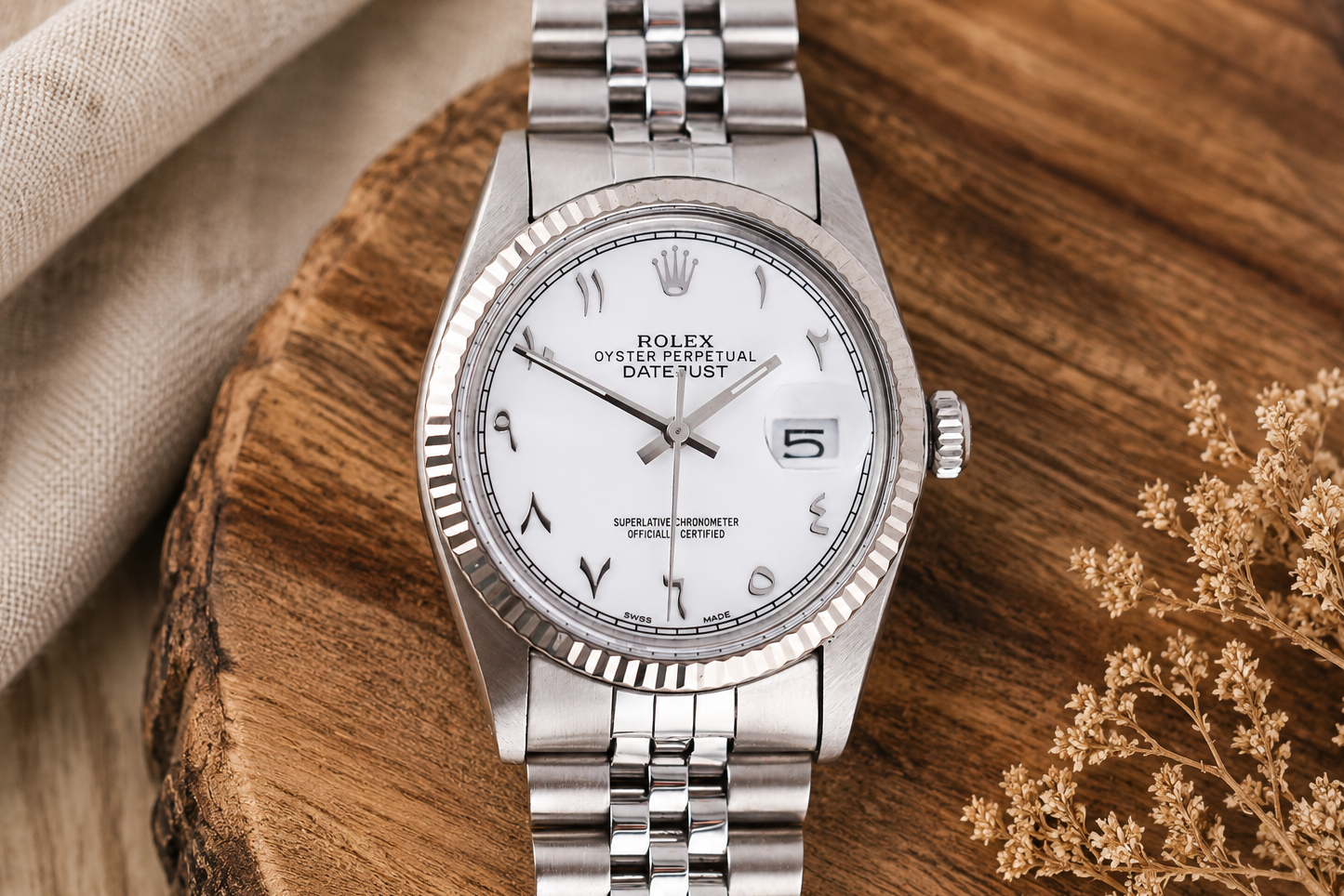 Silver Rolex watch on a wooden surface with a neutral background