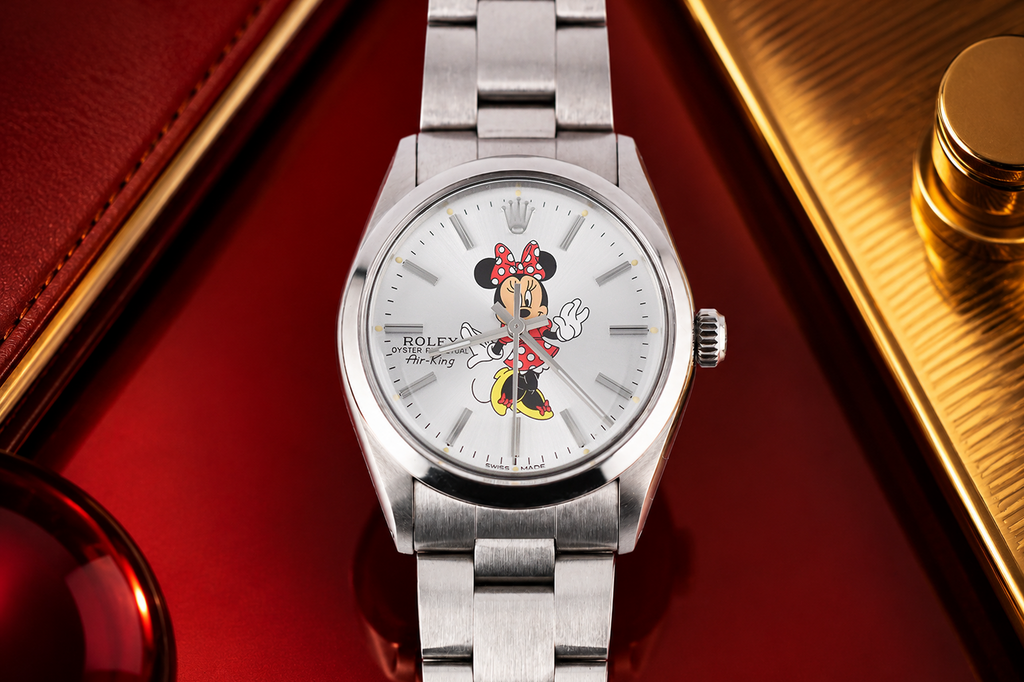 Silver watch with Minnie Mouse design on the dial, placed on a red surface with gold accents.