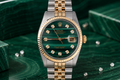 Luxury watch with green dial and gold and silver band on a green marble surface