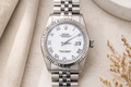 Silver Rolex watch with a white dial on a textured beige surface