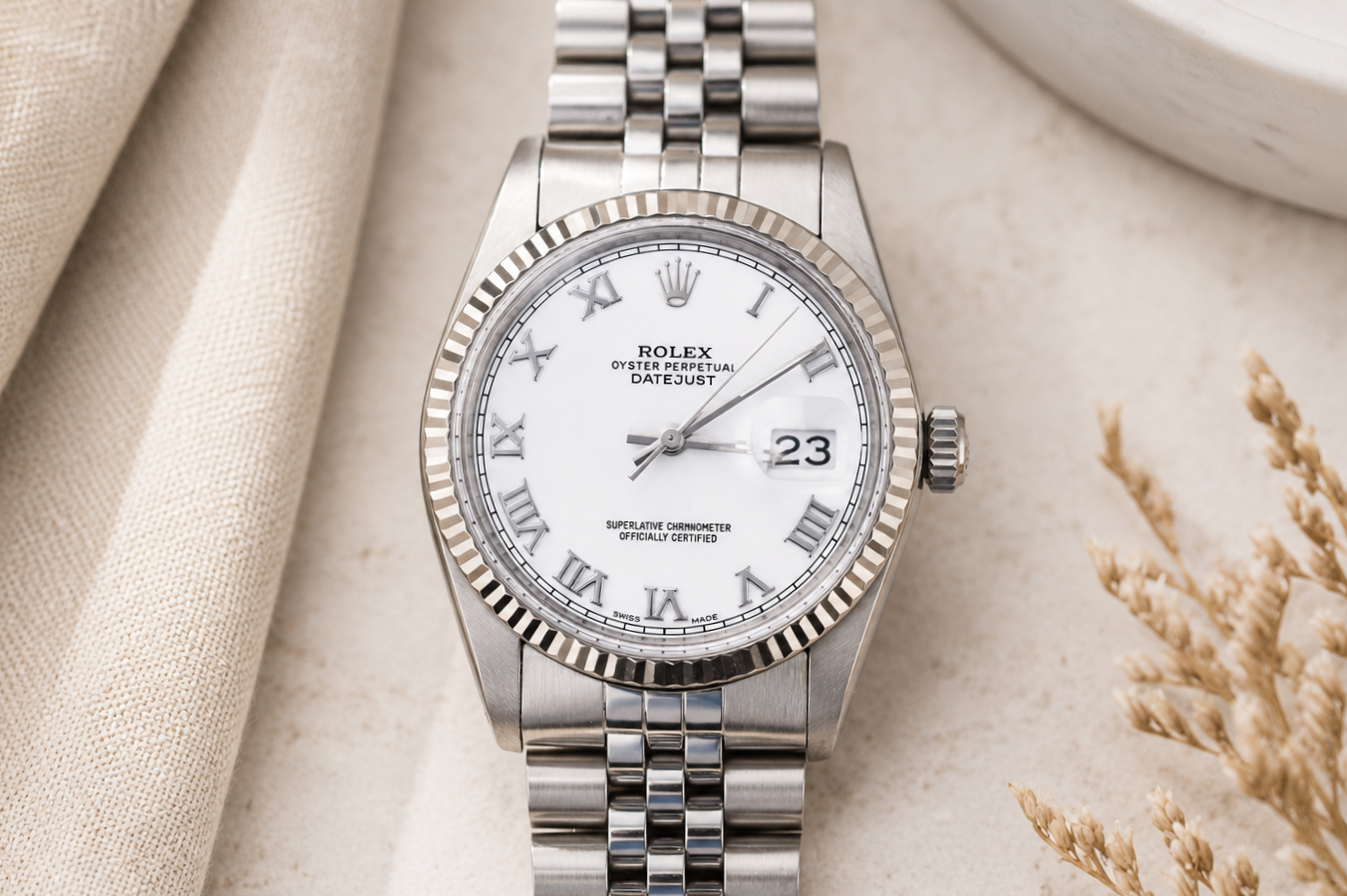 Silver Rolex watch with a white dial on a textured beige surface