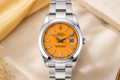 Silver watch with orange face on a beige surface with flowers