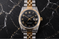 Luxury watch with black dial and gold accents on a black marble background