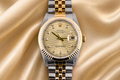 Luxury two-tone watch with gold and silver straps on a gold fabric background