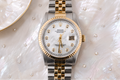 Rolex watch with silver and gold band on a textured white surface