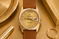 Gold watch with brown leather strap on a gold surface