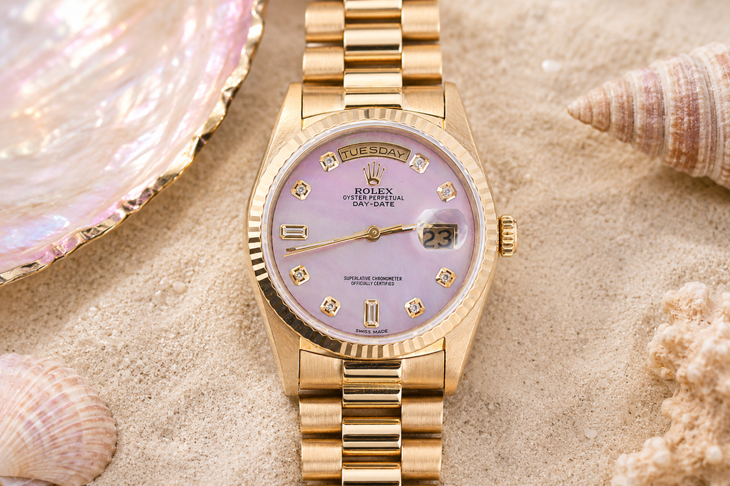 Gold watch with a pink face on sand with shells