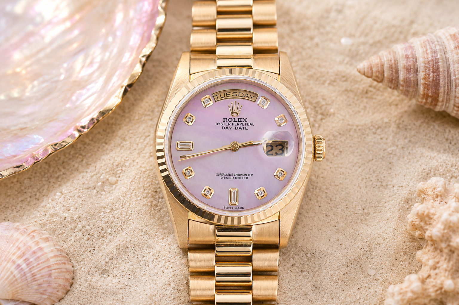 Gold watch with a pink face on sand with shells