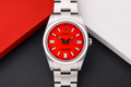 Silver watch with a red face on a dark surface with a red and white background