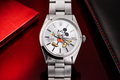 Silver watch with a Mickey Mouse design on the dial, placed on a red surface.