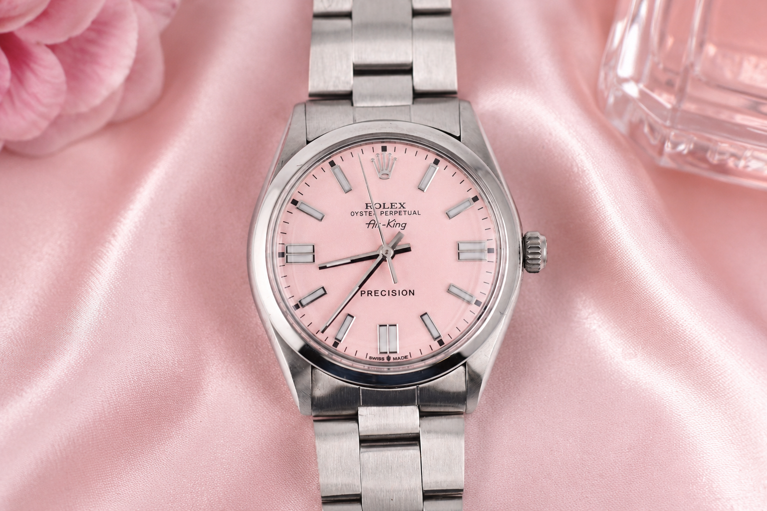 Silver watch with a pink face on a pink fabric background