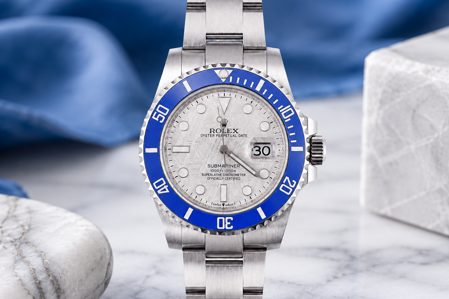 Silver watch with blue bezel on a marble surface with blue fabric background