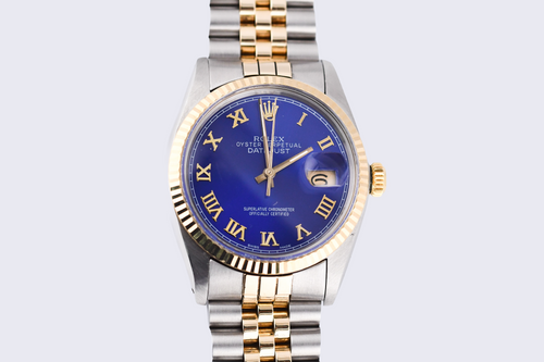 Luxury watch with blue dial and gold and silver band on light gray background