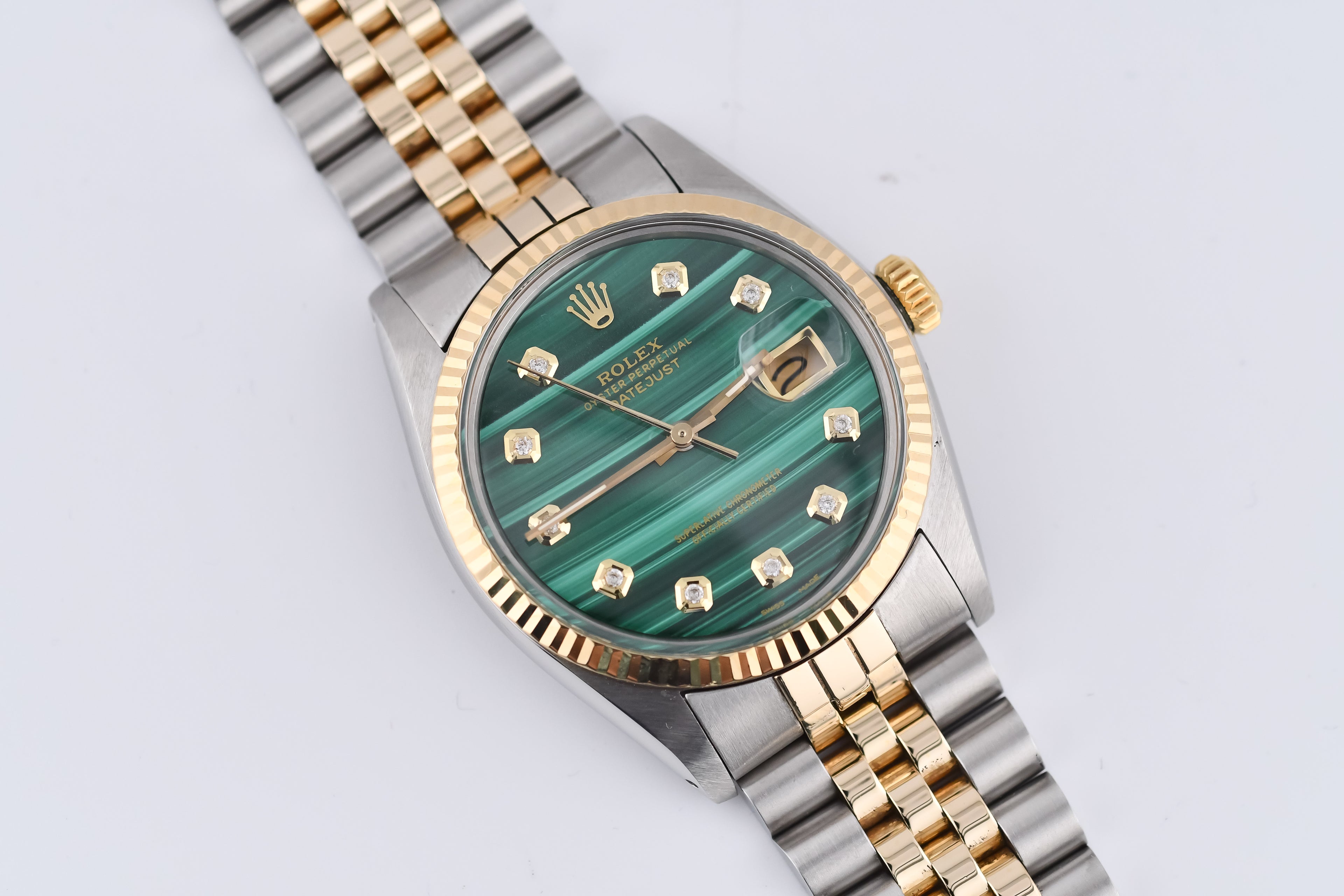 Luxury watch with green face and gold and silver band on light gray background
