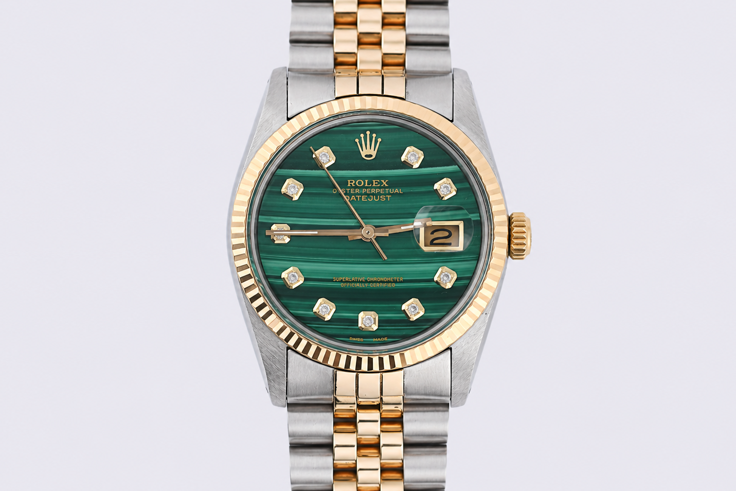 Rolex watch with green face and gold and silver band on light gray background