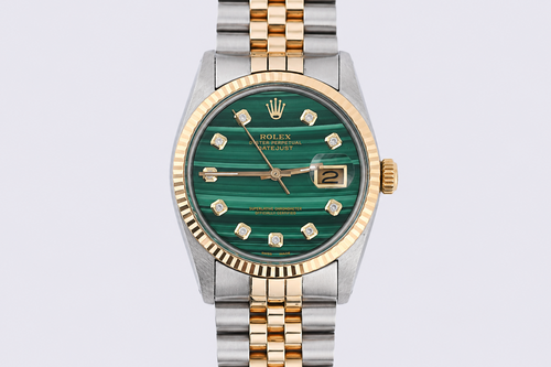 Rolex watch with green face and gold and silver band on light gray background