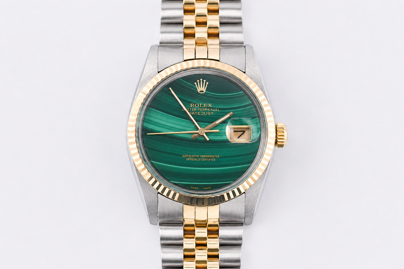 Luxury watch with green face and gold and silver band on light gray background