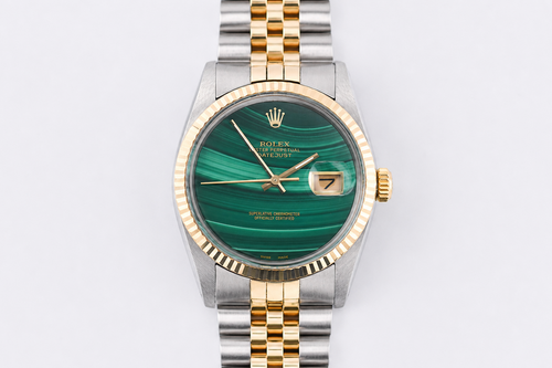 Luxury watch with green face and gold and silver band on light gray background