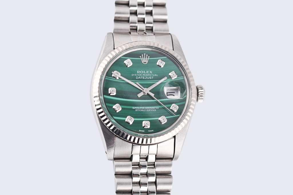 Silver watch with a green face on a light gray background