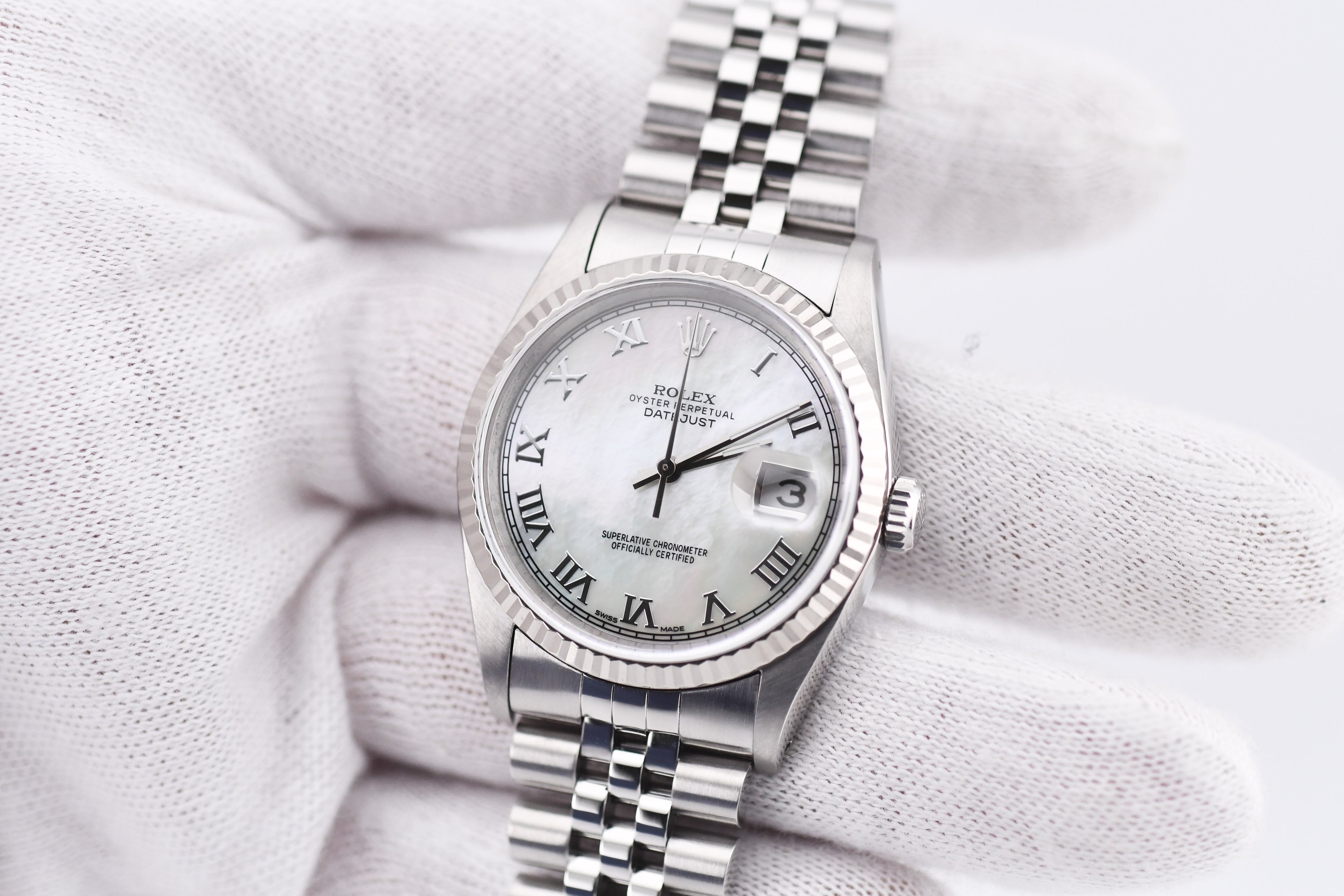 Silver watch with a white face on a textured white background