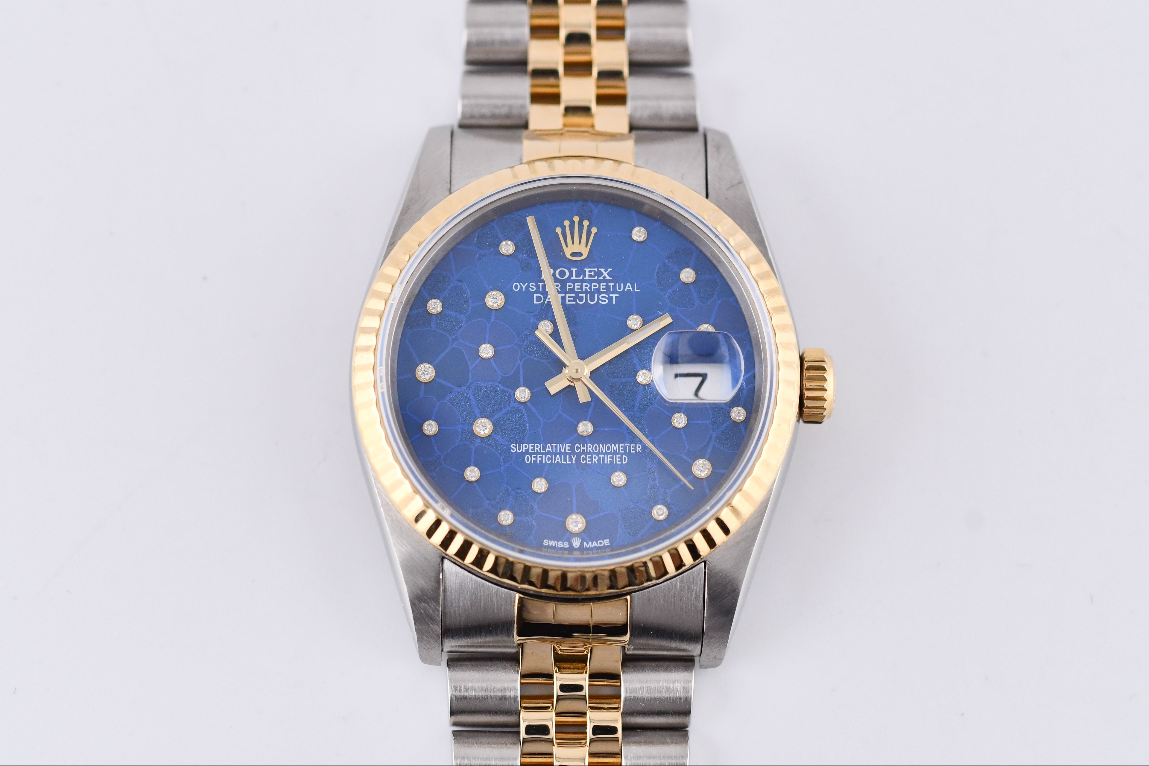 Rolex watch with blue dial and gold and silver band on a light gray background