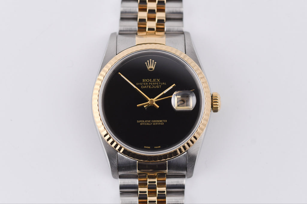 Rolex watch with black dial and gold accents on a light gray background