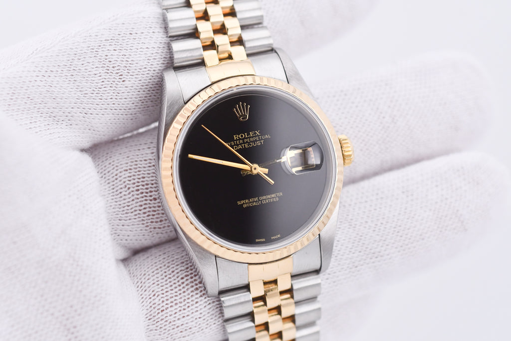 Luxury watch with black dial and gold and silver band on a light fabric background