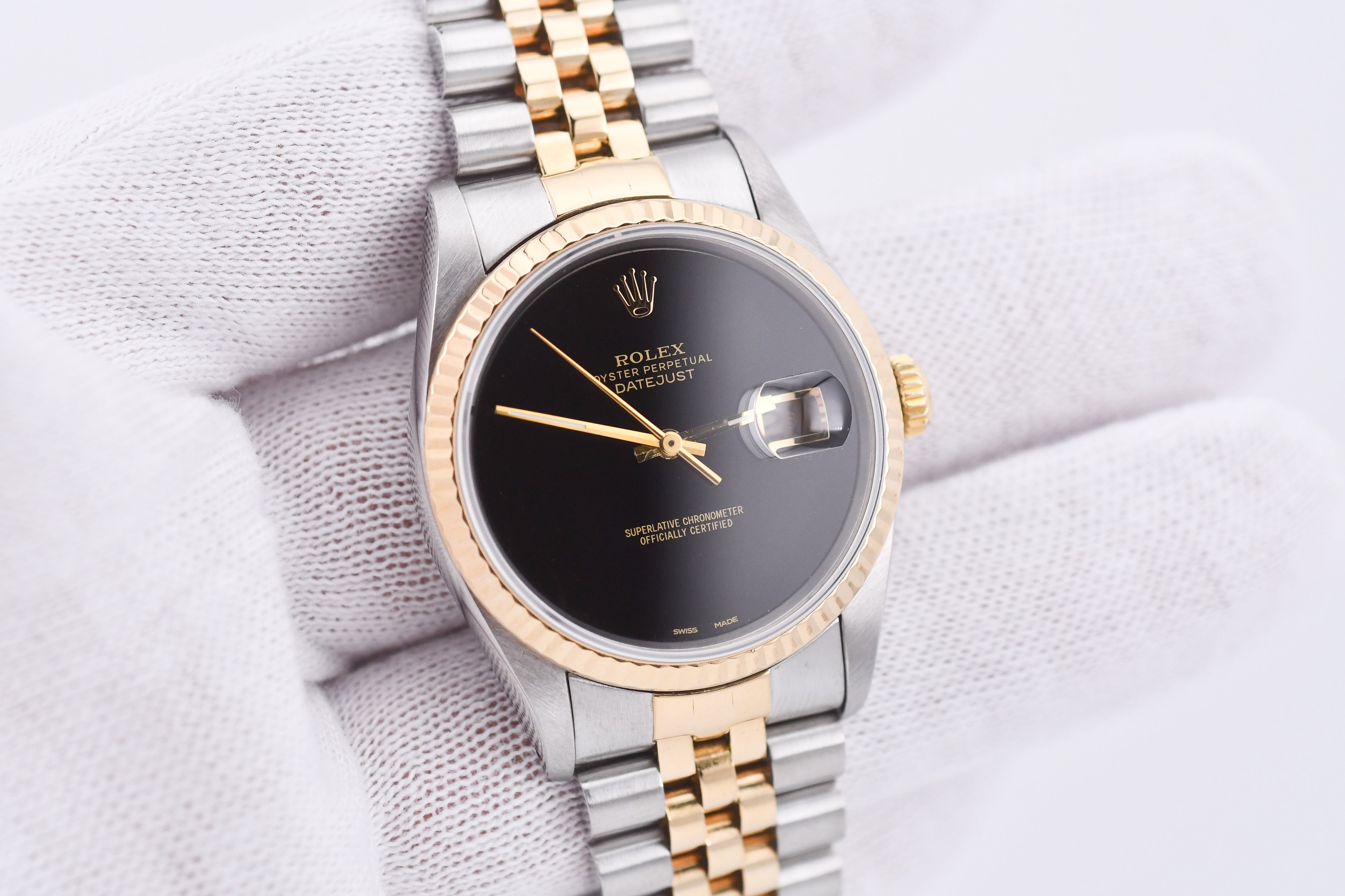 Luxury watch with black dial and gold and silver band on a light fabric background