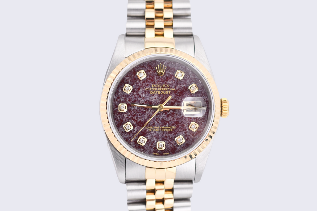 Luxury watch with a maroon face and gold accents on a light gray background