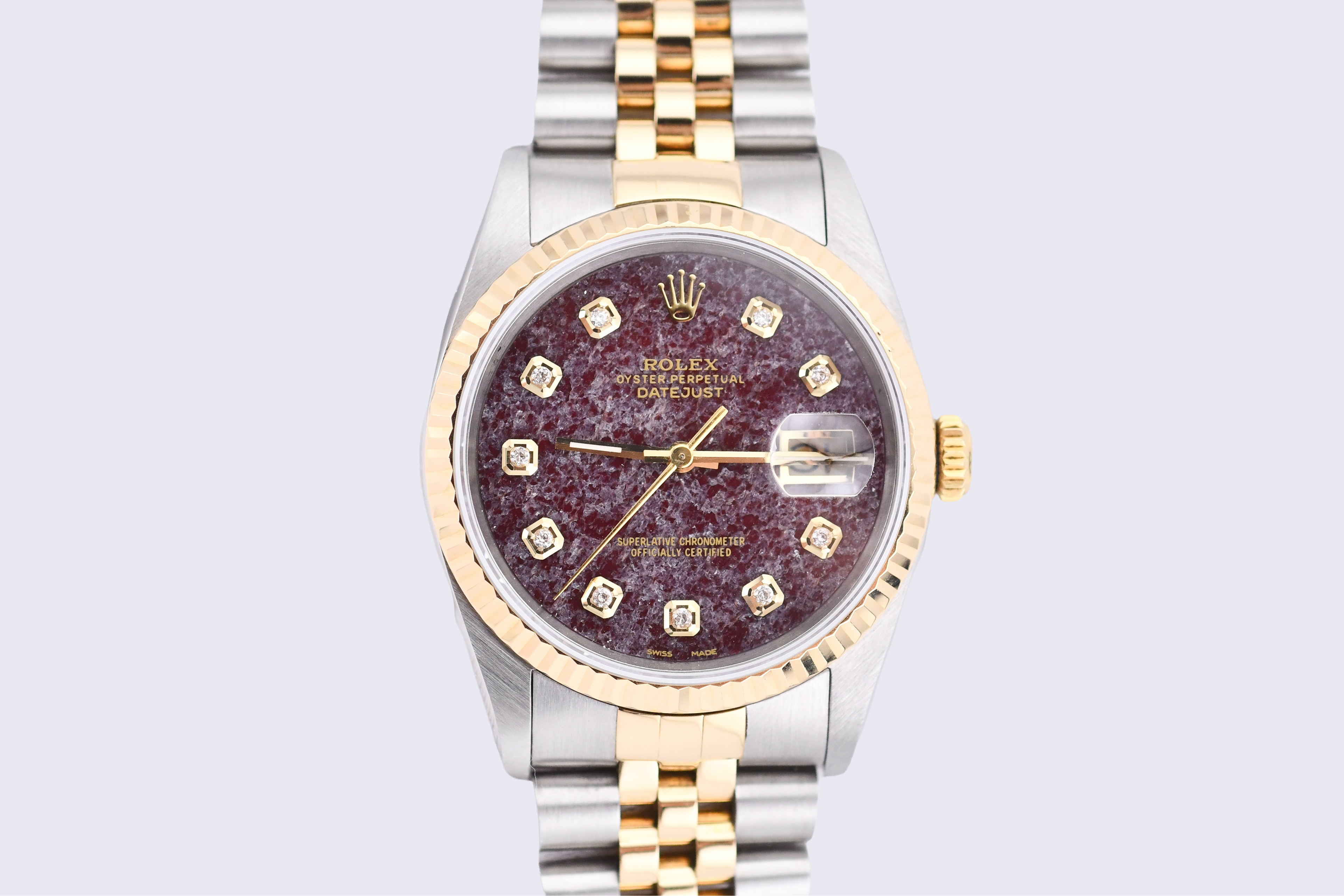 Luxury watch with a maroon face and gold accents on a light gray background